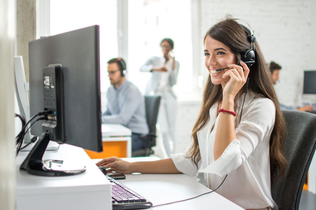 lady in call center holding a phone over her hear with the background of other colleagues(about)